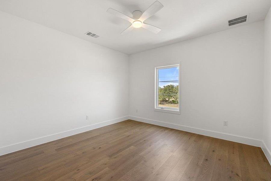 A well-lit room featuring rich hardwood flooring and a functional ceiling fan for comfort.