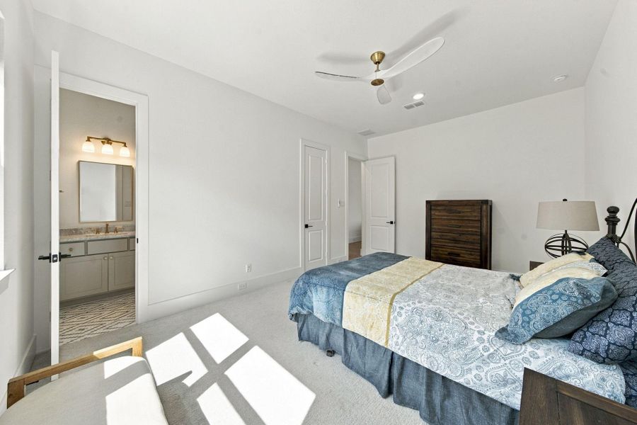 Another view of this bright secondary bedroom highlights direct access to its private bath. Soft carpet flooring and a ceiling fan complete this comfortable space.