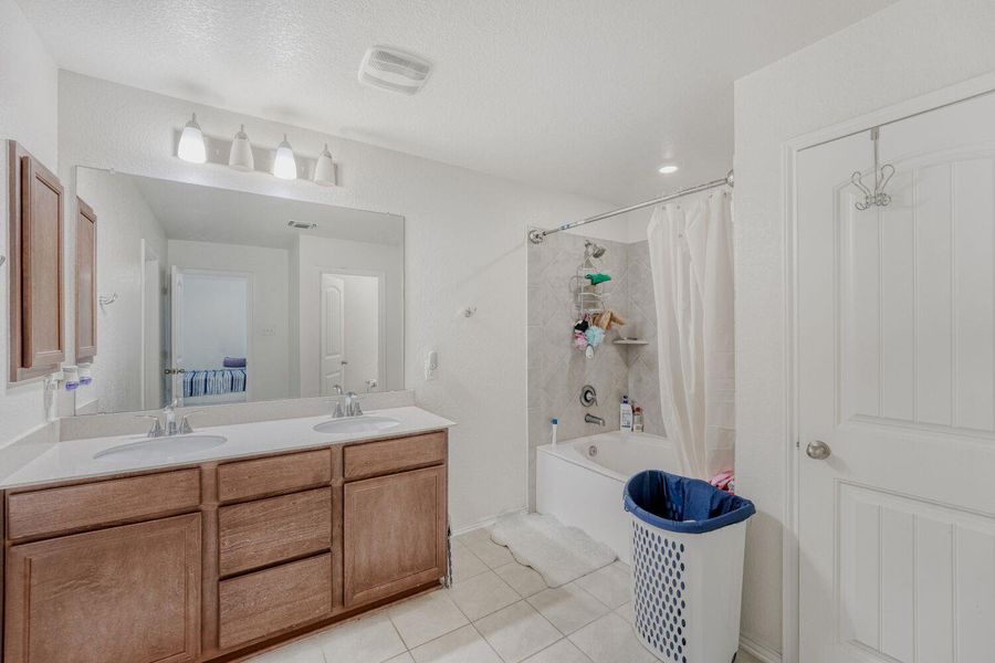 Bathroom featuring shower / bath combination with curtain, double vanity, light tile patterned floors, ensuite bath, and a textured ceiling