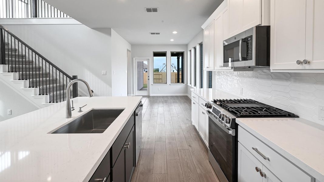 Kitchen featuring dark cabinetry, appliances with stainless steel finishes, white cabinets, wood finished floors, and light stone countertops Kitchen featuring dark cabinetry, appliances with stainless steel finishes, white cabinets, wood finished floors, and light stone countertops