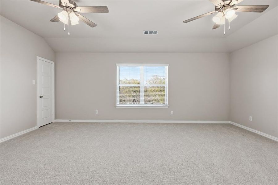 Spacious room featuring neutral carpeting, a large window with blinds, two ceiling fans with integrated lighting, and a paneled door