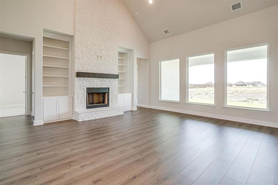 Unfurnished living room featuring hardwood / wood-style flooring, a stone fireplace, built in features, and high vaulted ceiling