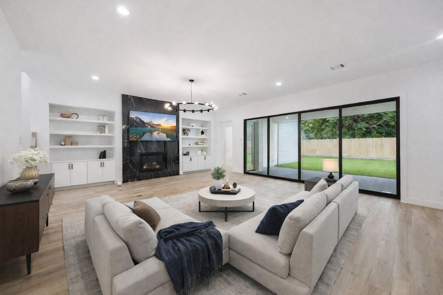 Expansive and bright, the living room features a dramatic black marble fireplace flanked by custom built-ins, wide-plank floors, and a statement light fixture. A full wall of sliding glass doors opens to the covered patio, creating a seamless indoor-outdoor connection perfect for entertaining. *Virtually Staged* Expansive and bright, the living room features a dramatic black marble fireplace flanked by custom built-ins, wide-plank floors, and a statement light fixture. A full wall of sliding glass doors opens to the covered patio, creating a seamless indoor-outdoor connection perfect for entertaining. *Virtually Staged*