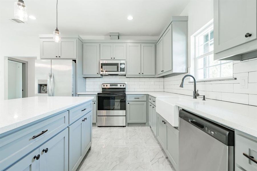 Kitchen featuring backsplash, stainless steel appliances, decorative light fixtures, light stone counters, and light tile patterned flooring