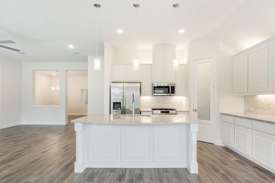 White kitchen with large center island, granite countertops, stainless steel appliances, and pendant lights over wood-look floors