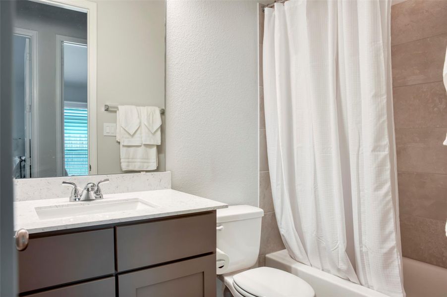 This bathroom features a modern vanity with a marble countertop, a sleek faucet, and ample cabinet space. It includes a toilet and a bathtub with a white shower curtain. The light-colored tiles and neutral tones create a clean, bright atmosphere. This bathroom features a modern vanity with a marble countertop, a sleek faucet, and ample cabinet space. It includes a toilet and a bathtub with a white shower curtain. The light-colored tiles and neutral tones create a clean, bright atmosphere.