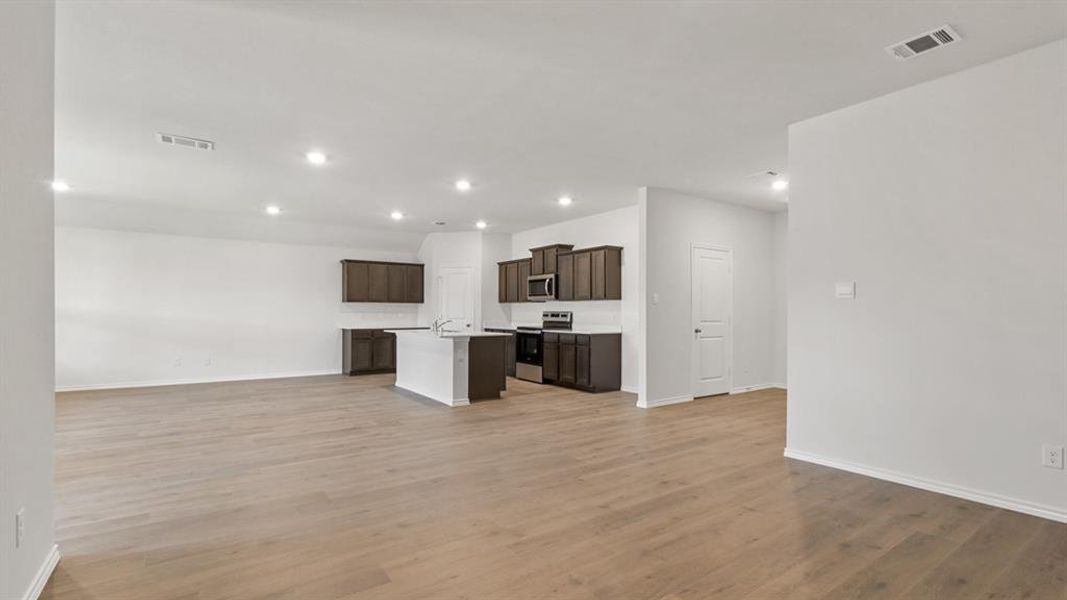 Kitchen featuring open floor plan, an island with sink, light countertops, stainless steel appliances, and dark wood finish cabinets
