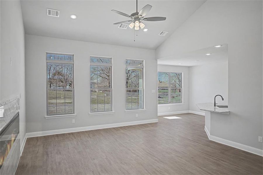 Unfurnished living room featuring light wood-style floors, a ceiling fan, vaulted ceiling, a glass covered fireplace, and recessed lighting