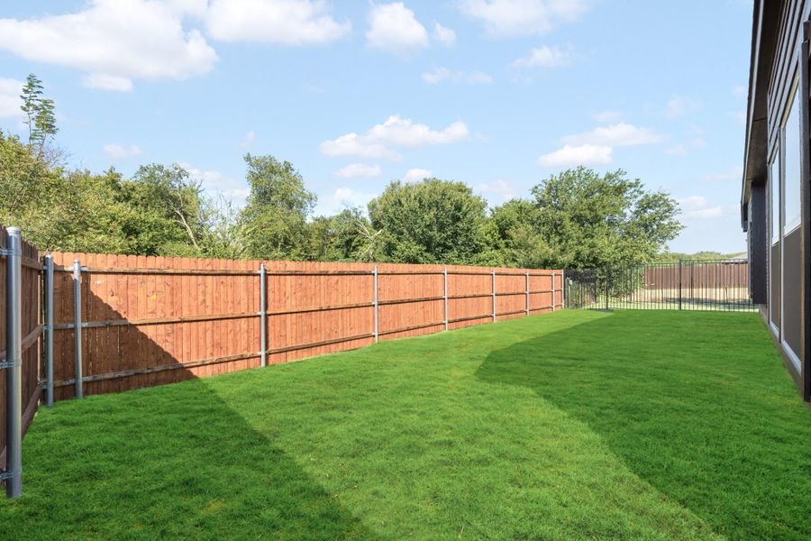 Backyard with green grass lawn enclosed by a wood privacy fence and wrought iron gate