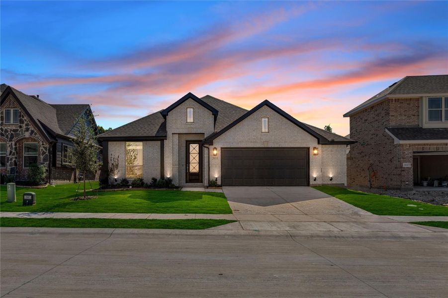 Single-story home with light brick exterior, two-car garage, and green front lawn at dusk Single-story home with light brick exterior, two-car garage, and green front lawn at dusk