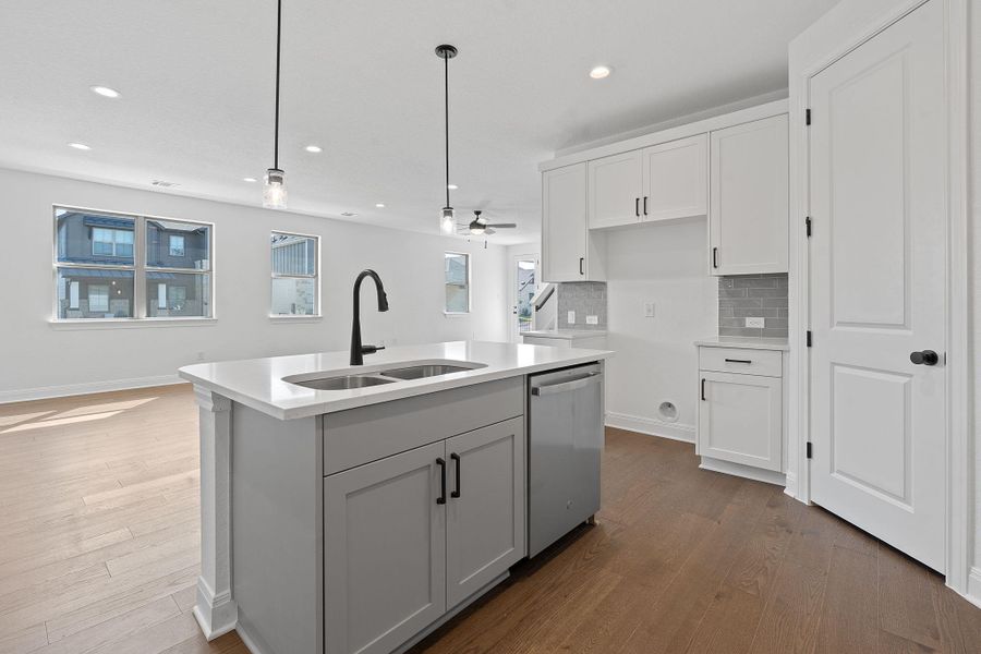 Kitchen featuring white cabinets, tasteful backsplash, stainless steel dishwasher, decorative light fixtures, and a kitchen island with sink Kitchen featuring white cabinets, tasteful backsplash, stainless steel dishwasher, decorative light fixtures, and a kitchen island with sink