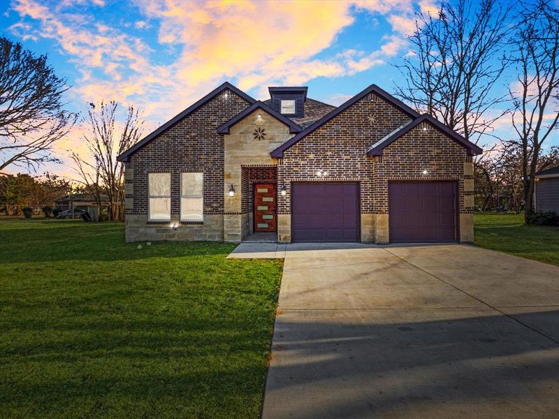 French country home featuring a garage, concrete driveway, brick siding, stone siding, and a front yard French country home featuring a garage, concrete driveway, brick siding, stone siding, and a front yard