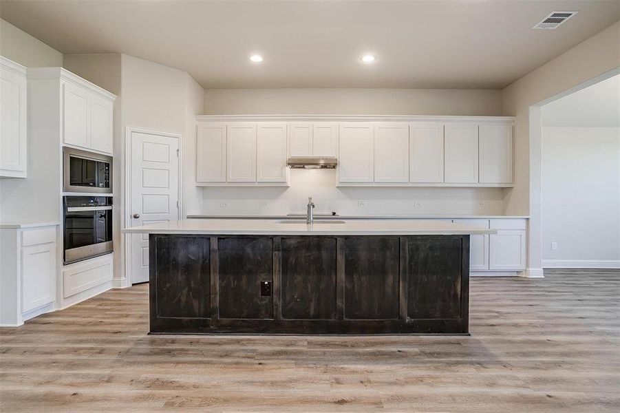 Kitchen featuring stainless steel appliances, sink, a center island with sink, white cabinets, and light hardwood / wood-style floors