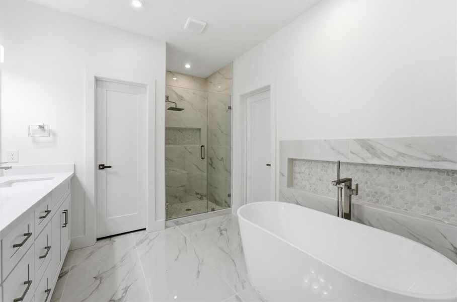 Spa-inspired primary bath featuring a freestanding soaking tub, glass-enclosed shower, and marble-look tile.