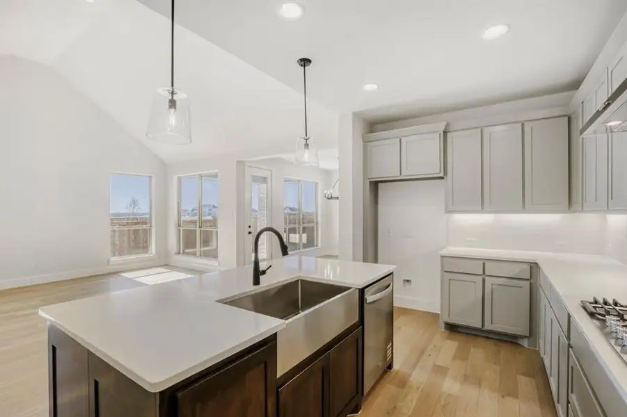 Dual tone kitchen featuring light wood-style floors, a kitchen island with sink, vaulted ceiling, hanging light fixtures, and stainless steel appliances