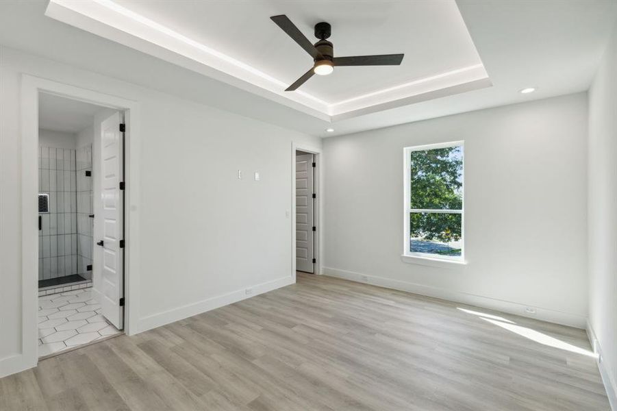 Bedroom with light wood-type flooring, ceiling fan, and a raised ceiling