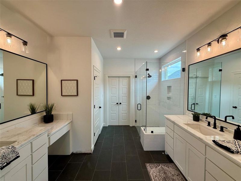 Spacious bathroom featuring twin vanities with stone countertops, a large glass-enclosed shower with white subway tile, dark tile flooring, and matte black fixtures