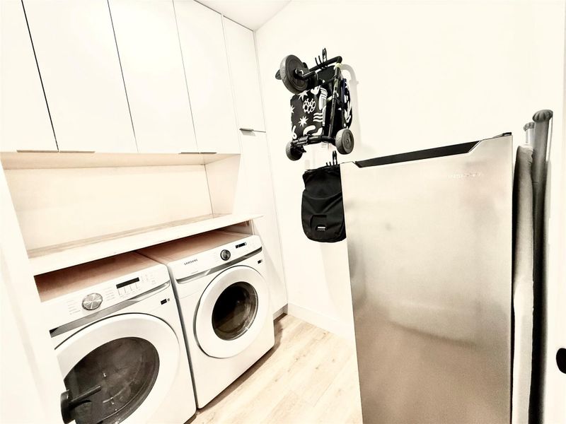 Washroom with independent washer and dryer, cabinet space, and light wood-style floors