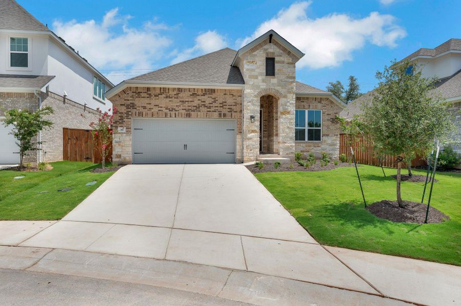 French country inspired facade with stone siding, a shingled roof, driveway, brick siding, and an attached garage