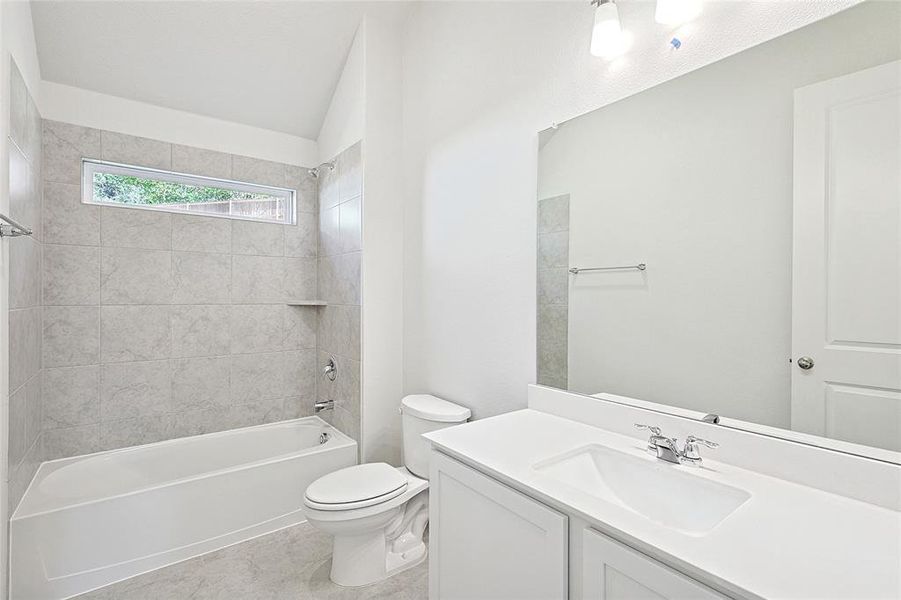 Full bathroom featuring tile patterned floors, vanity, tiled shower / bath combo, vaulted ceiling, and toilet