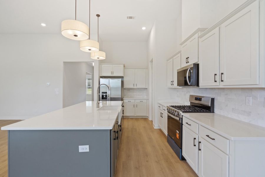 Kitchen featuring a large central island, white cabinetry with dark hardware, stainless steel appliances, and wood-finish flooring