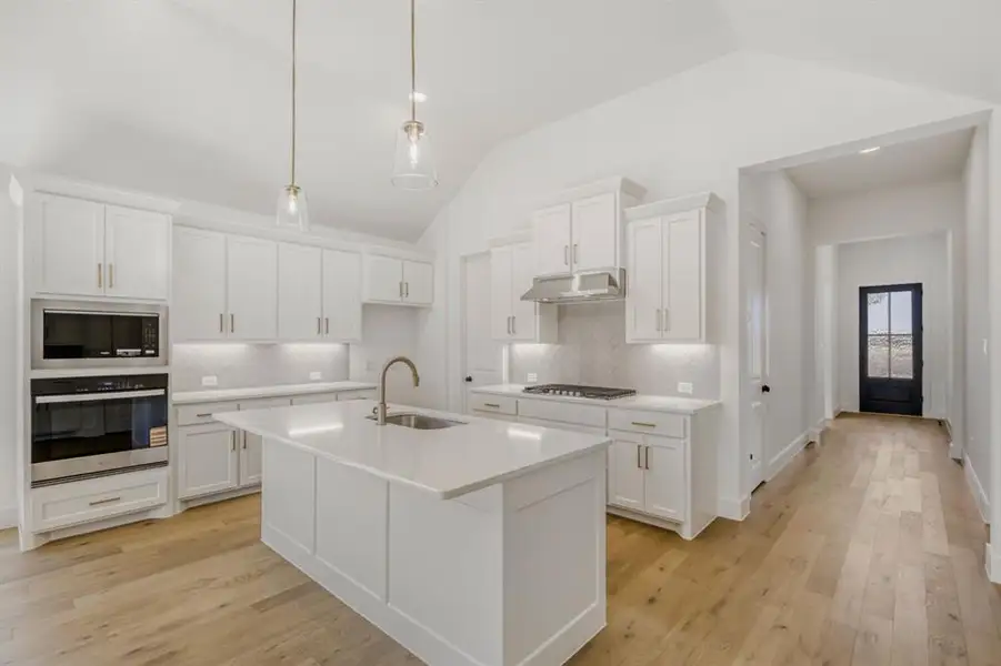 Kitchen with white cabinetry, stainless steel appliances, an island with sink, light wood-type flooring, and tasteful backsplash