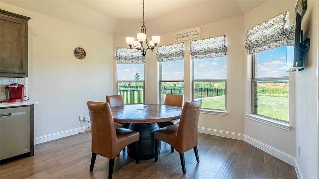 Bright dining area featuring wood-finish flooring, a contemporary chandelier, and a bay window with multiple panes offering expansive outdoor scenery