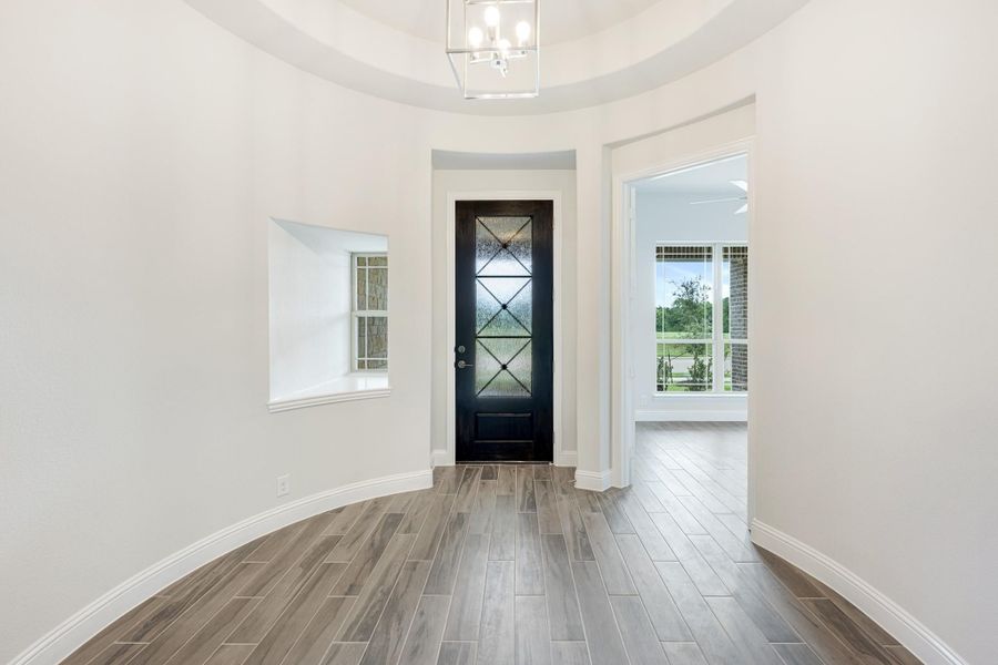 Curved foyer entry with dark glass-panel front door, chandelier, and wood-look tile floors