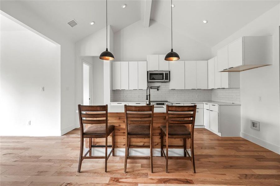 Kitchen with stainless steel microwave, light countertops, a kitchen island with sink, backsplash, and beam ceiling