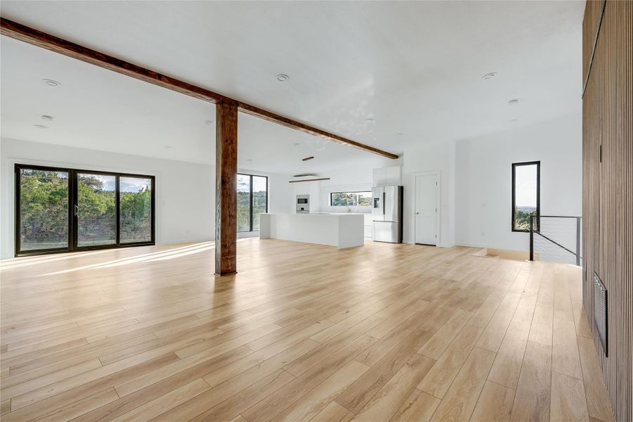 Unfurnished living room featuring beam ceiling, plenty of natural light, and light wood-style floors Unfurnished living room featuring beam ceiling, plenty of natural light, and light wood-style floors