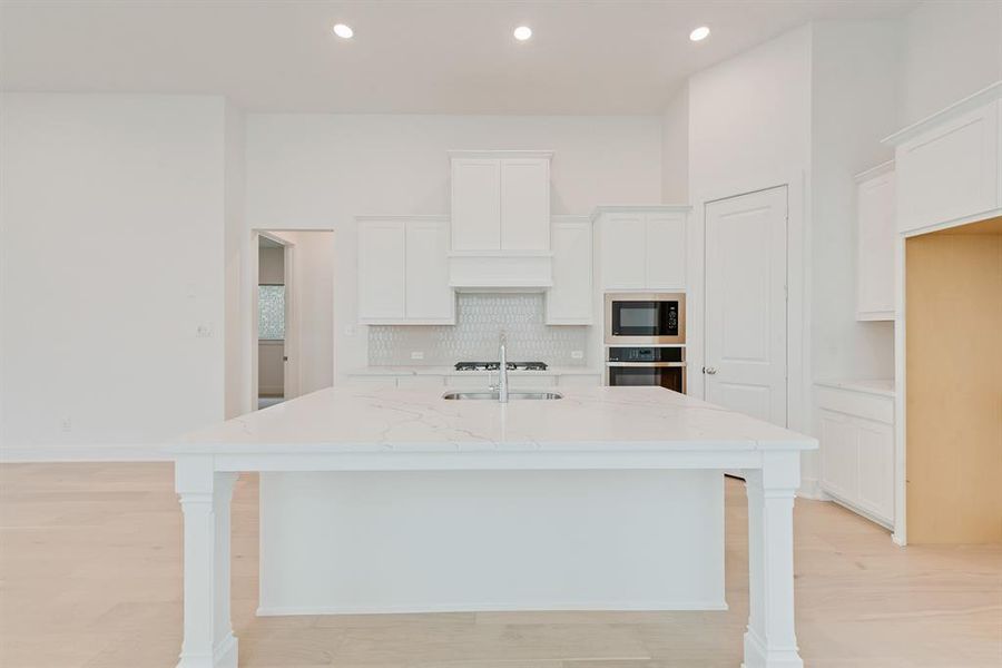 Kitchen featuring light stone counters, white cabinetry, decorative backsplash, an island with sink, and recessed lighting Kitchen featuring light stone counters, white cabinetry, decorative backsplash, an island with sink, and recessed lighting
