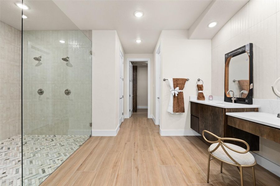 Bathroom featuring light wood-type flooring, a walk in shower, two vanities, and recessed lighting