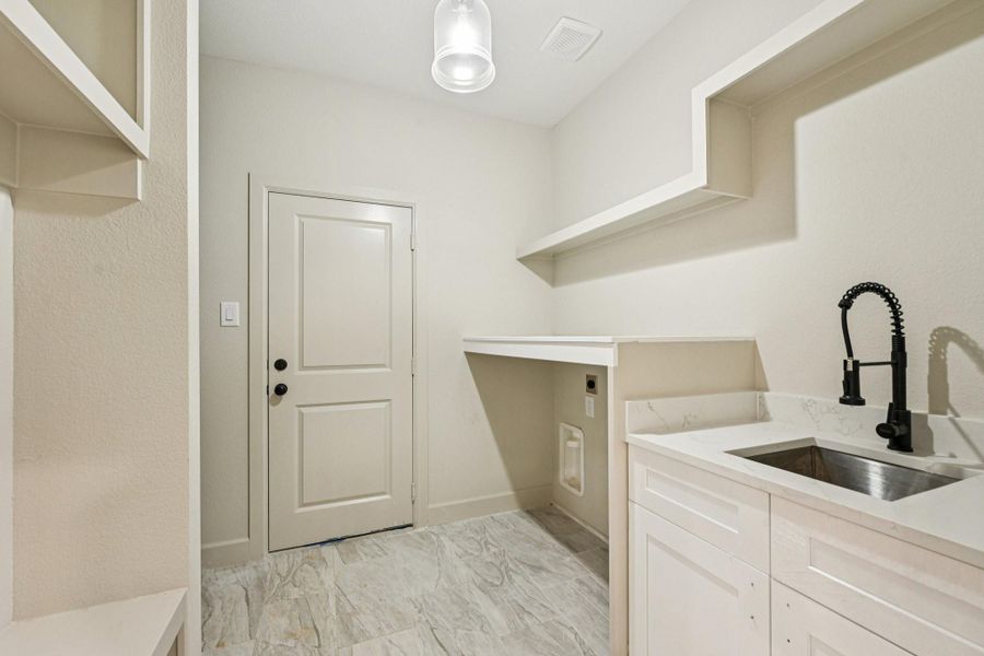This is a modern laundry room featuring a utility sink with a sleek faucet, ample countertop space, and shelving for storage.