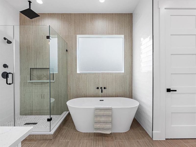 The primary bathroom showcases floor-to-ceiling tile in the stand-up shower, complemented by two shower heads. The soaking tub is elegantly designed with perfect natural lighting.