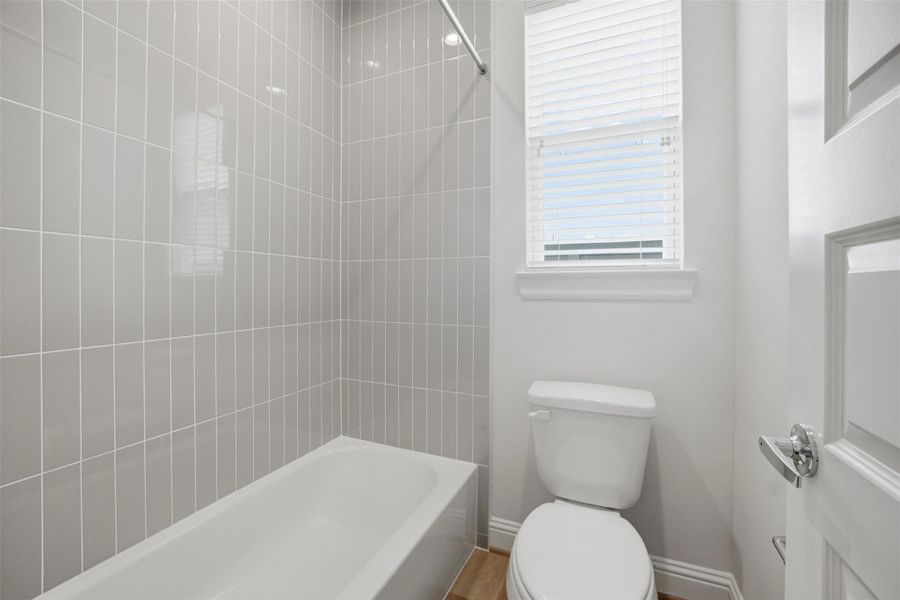 Bright and inviting, this guest bathroom features sleek gray tile, a modern bathtub, and abundant natural light for a refreshing experience.