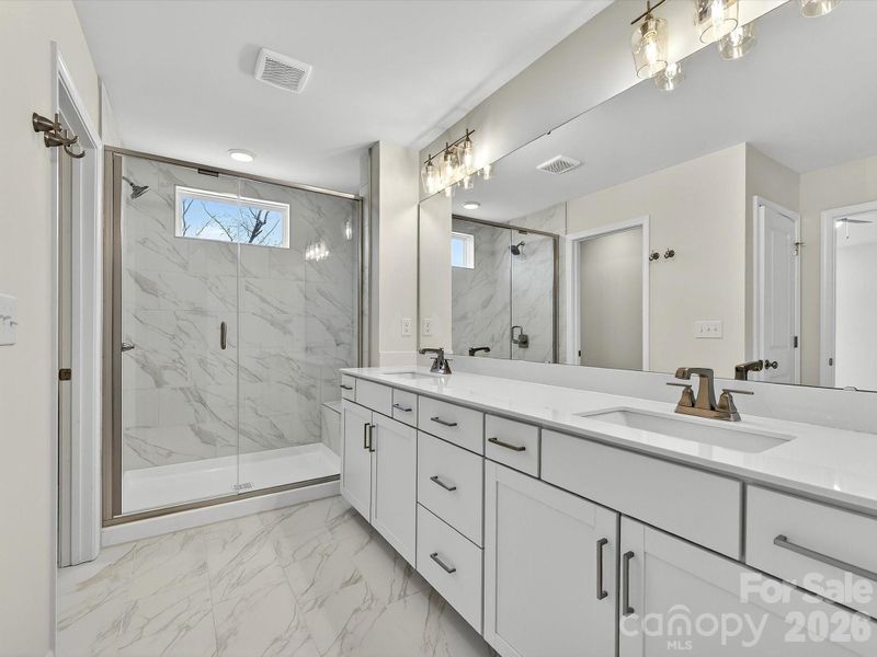 owners' bath with oversized dual vanity, with soft close doors and drawers, quartz countertops leading to large primary closet. Large, tiled shower with bench.