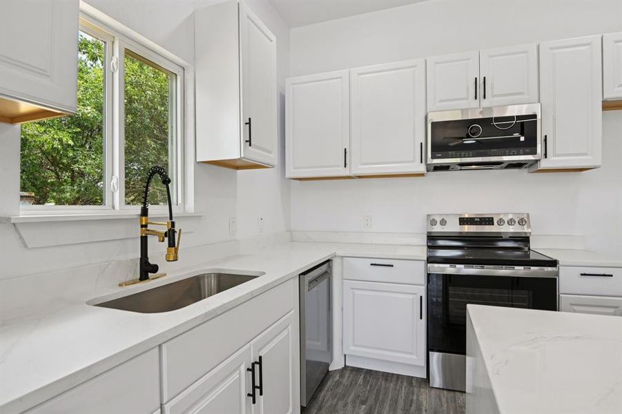 Kitchen with stainless steel appliances, light stone countertops, white cabinetry, and dark wood-style floors Kitchen with stainless steel appliances, light stone countertops, white cabinetry, and dark wood-style floors