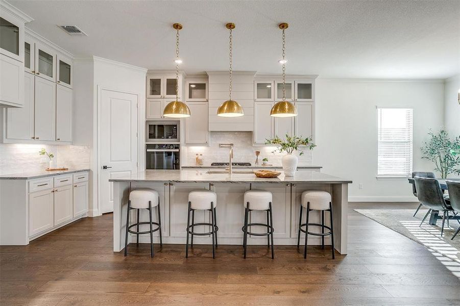 Kitchen featuring a large island, Quartzite countertops, gold hardware, decorative light fixtures, custom cabinetry to the ceiling, gas cooktop, double oven and walk in pantry