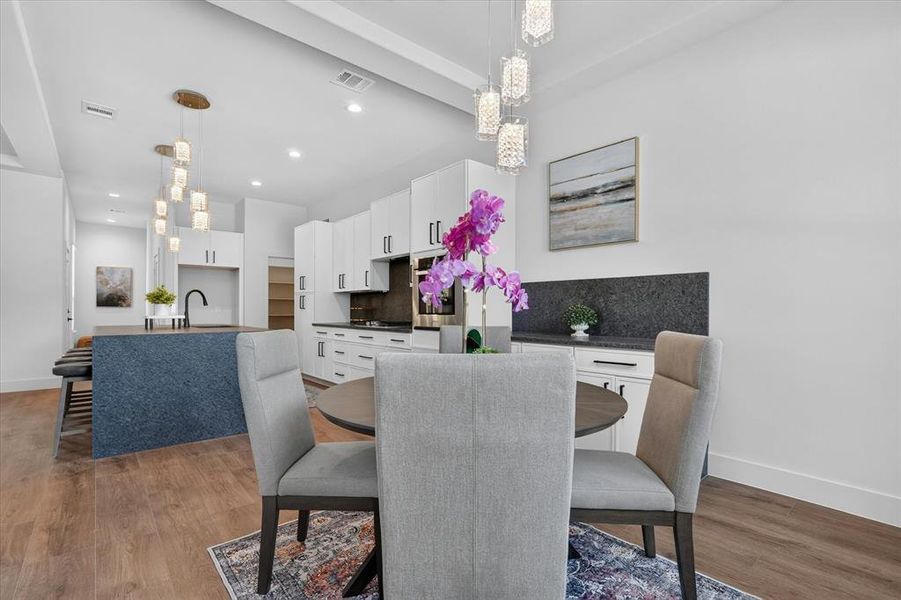 Spacious dining area with wood-finish flooring, complemented by a modern kitchen featuring white cabinetry and dark countertops