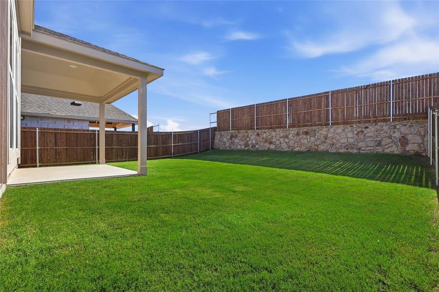 Expansive backyard with a covered patio, manicured lawn, full privacy fencing, and a stone retaining wall