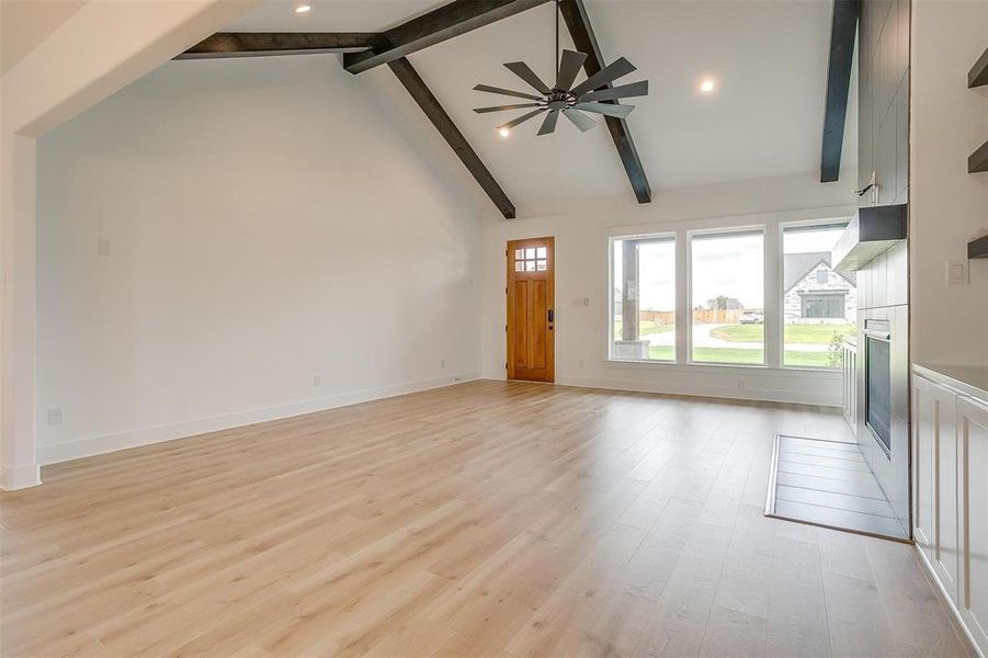 Unfurnished living room featuring beamed ceiling, high vaulted ceiling, ceiling fan, and light hardwood / wood-style floors