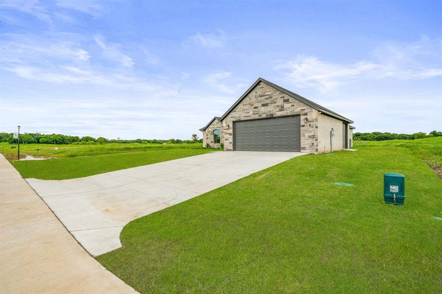 View of front of house featuring a front yard, driveway, stone siding, and a garage