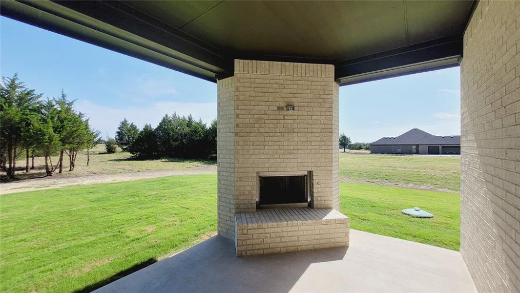 Covered patio featuring an outdoor brick fireplace, concrete flooring, and surrounding green space