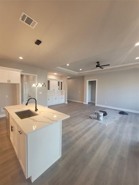 Kitchen featuring open floor plan, white cabinets, an island with sink, light stone counters, and recessed lighting