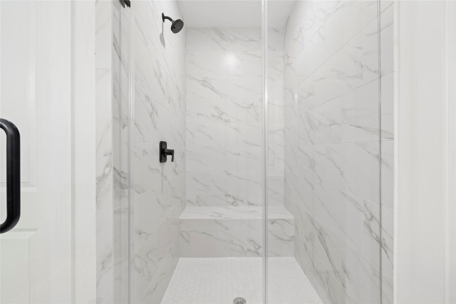 Featuring floor-to-ceiling marble-inspired tile, a sleek glass enclosure, and modern matte black fixtures for a spa-like experience.