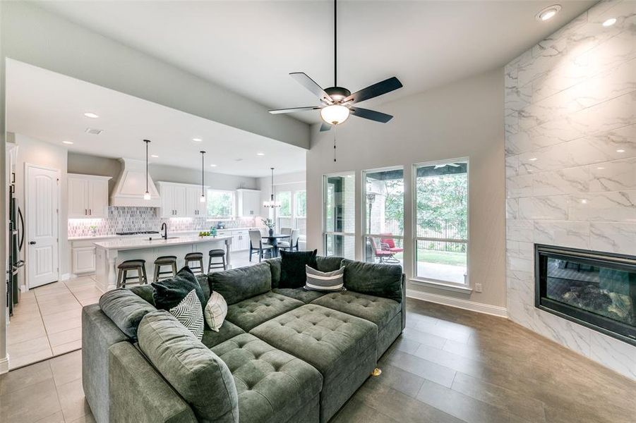 Living room with plenty of natural light, ceiling fan, a tiled fireplace, and light tile flooring