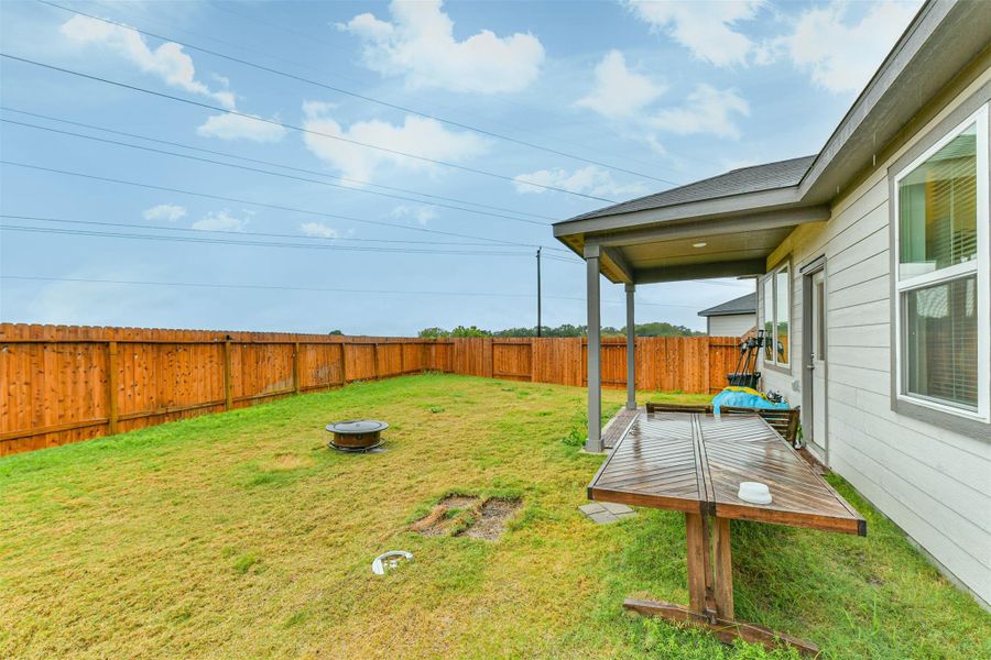 This photo showcases a spacious backyard with a well-maintained lawn, enclosed by a wooden fence. There's a covered patio attached to the house with no back neighbors. *The table, chairs, blow up house and fire pit will be removed*