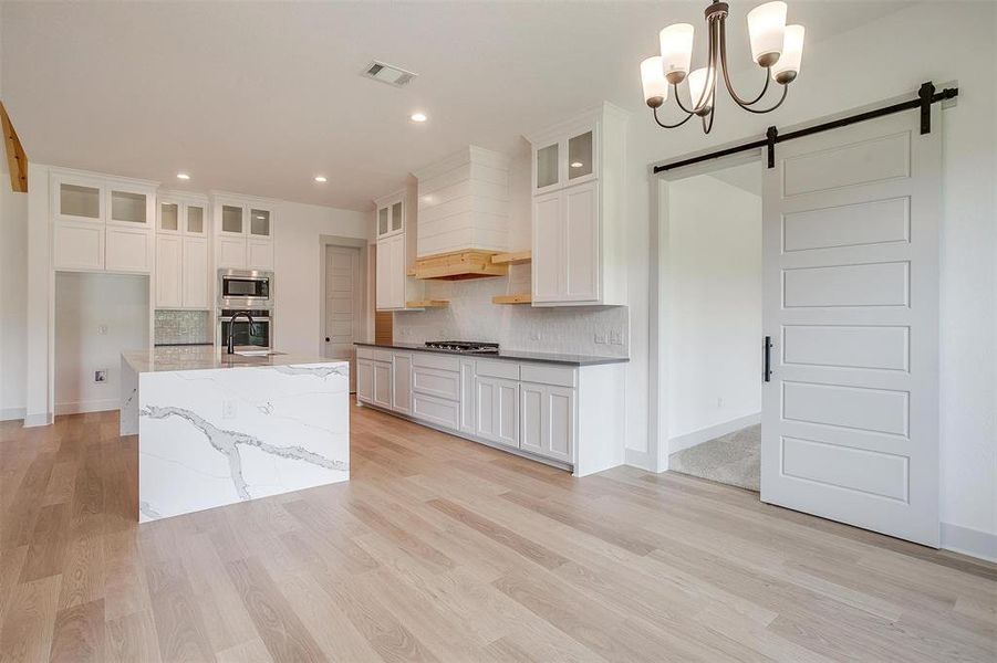 Kitchen featuring light hardwood / wood-style floors, a barn door, custom range hood, and decorative light fixtures