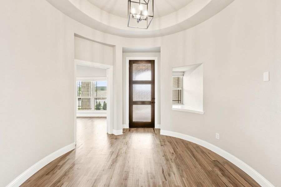 Circular foyer with tray ceiling, chandelier, dark wood front door with glass panels, and hardwood floors Circular foyer with tray ceiling, chandelier, dark wood front door with glass panels, and hardwood floors
