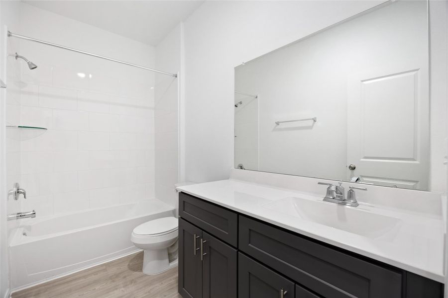 modern bathroom with a clean design, featuring a white bathtub with a shower, dark cabinetry, and a large mirror above the sink. The space is bright and contemporary, with light wood flooring.